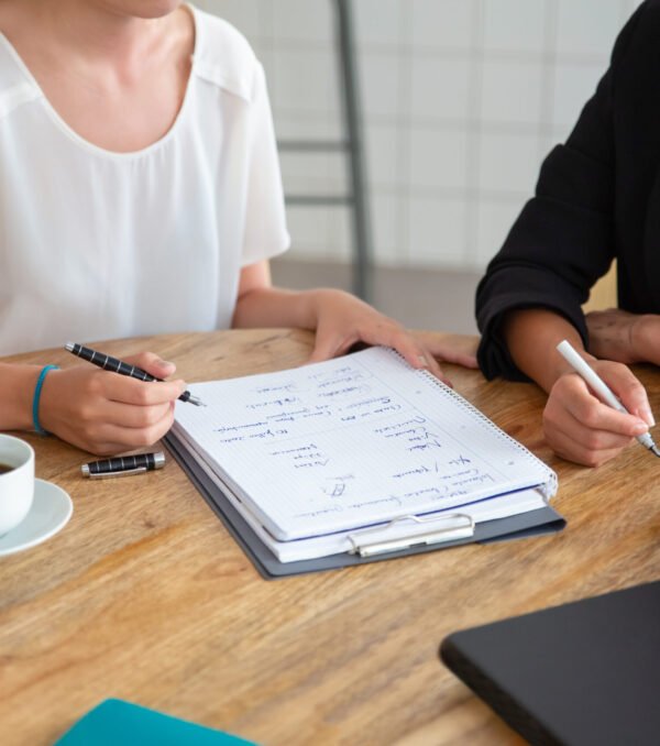 Young female colleagues meeting and discussing business plan, writing strategy scheme on paper, making draft. Cropped shot. Planning concept