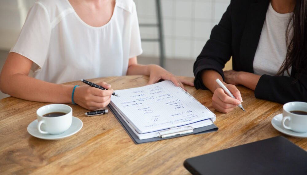 Young female colleagues meeting and discussing business plan, writing strategy scheme on paper, making draft. Cropped shot. Planning concept