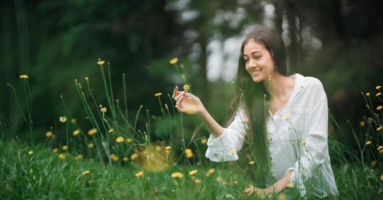 Mujer tocando algunas flores en un campo con pasto crecido.